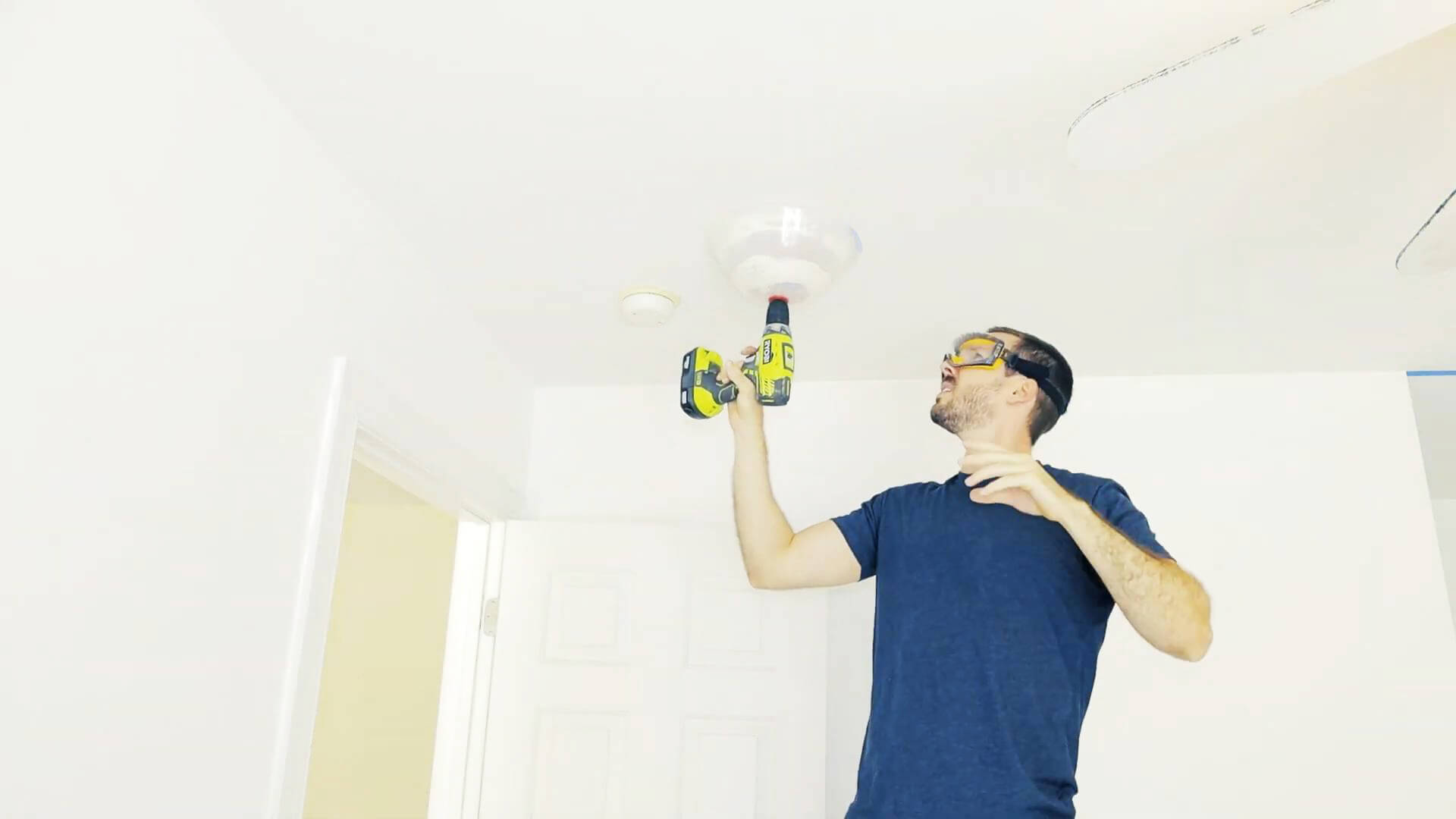 A person wearing safety glasses uses a drill to install a smart recessed light into a ceiling